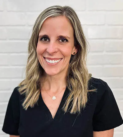 A professional, warm portrait of a female dentist in a modern dental office, smiling confidently at the camera in a white coat against a clean, beautifully designed background.