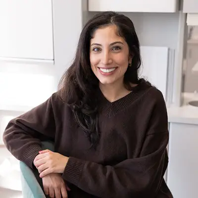 A warm, inviting dental office reception area with elegant lighting, fresh flowers on the front desk, and a smiling dental team member greeting a patient by name. The space feels intentionally designed — polished but personal.